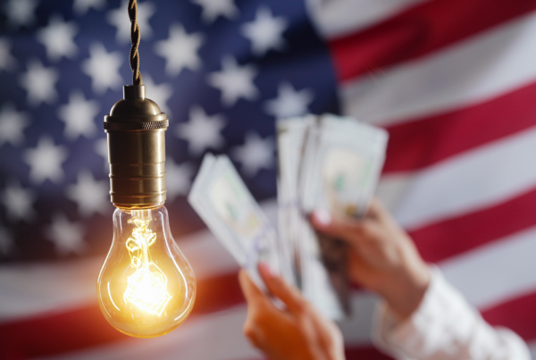 hands shown holding money with a light bulb in the foreground and an American flag in the background