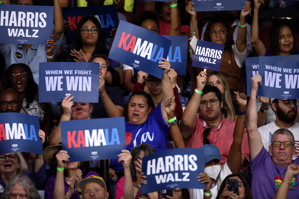 Crowd of people holding up Harris Walz campaign signs.