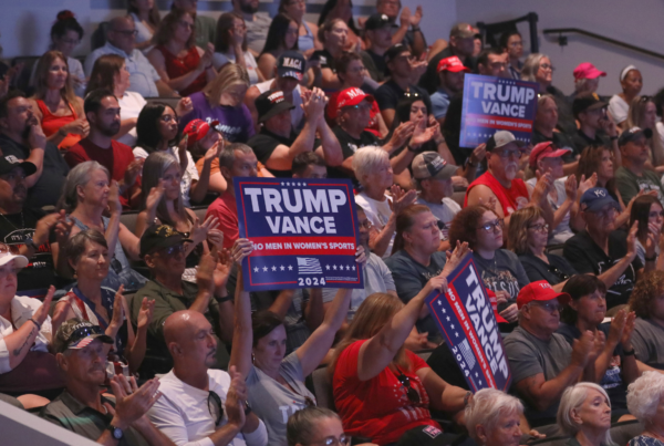 A crowd of people attending a political event. Some people are holding up Trump campaign signs.