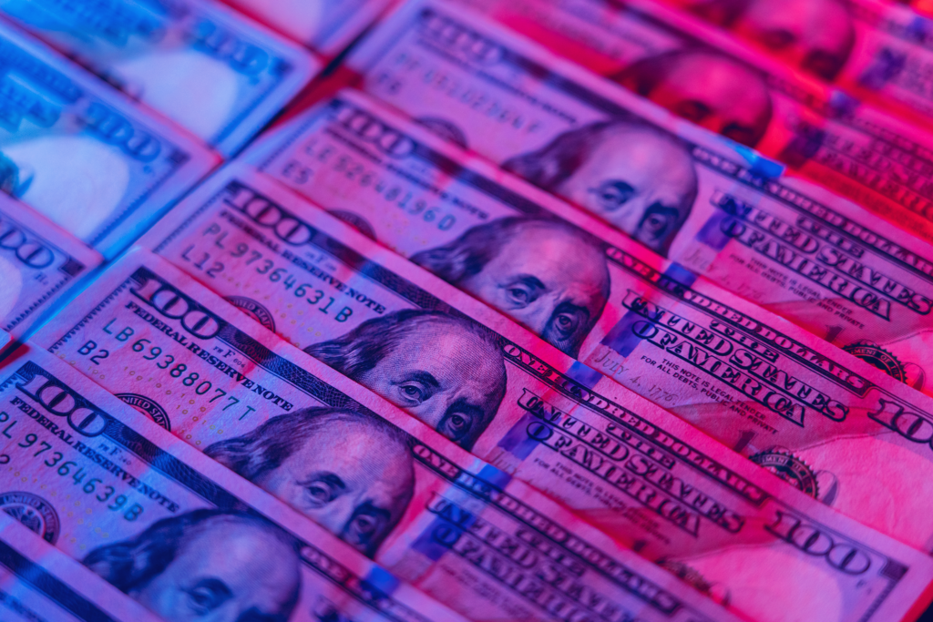 Hundred dollar bills with red and blue light shining down.