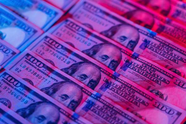 Hundred dollar bills with red and blue light shining down.