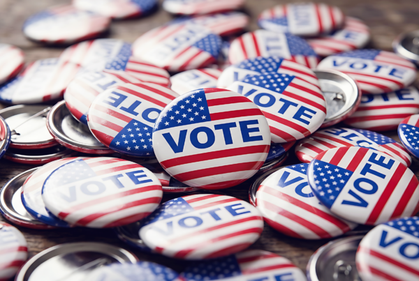 A pile a circular pins on a table. The pins have American flags and the word "vote" on them.